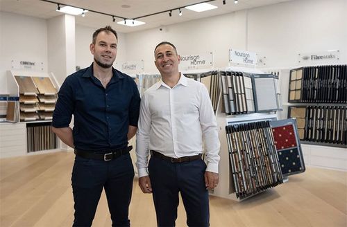 Two men standing in a flooring showroom with carpet and wood samples on display.