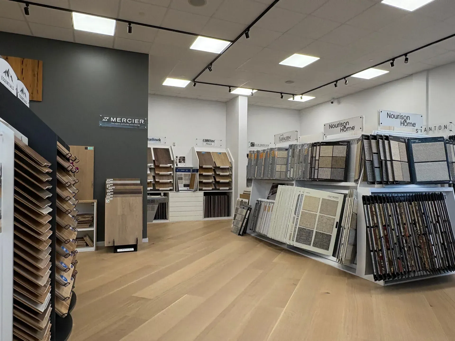 Empty flooring showroom with sample displays, light wood floors, and wall-mounted tile racks