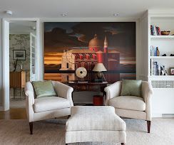 Elegant living room with two cream chairs, ottoman, lamp, and a large train mural on the wall