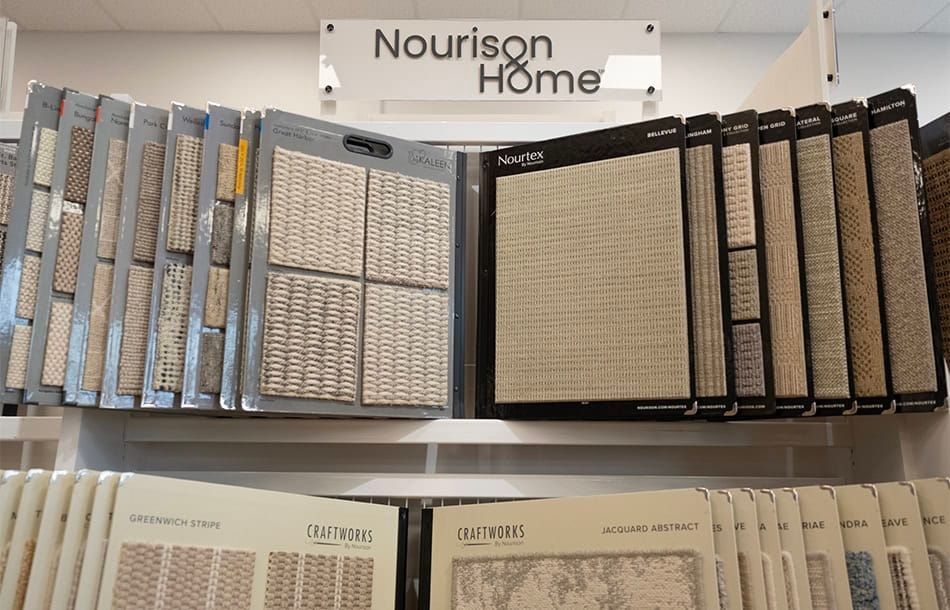 Display of Nourison Home carpet and rug samples on a store shelf, with assorted neutral-toned textures.