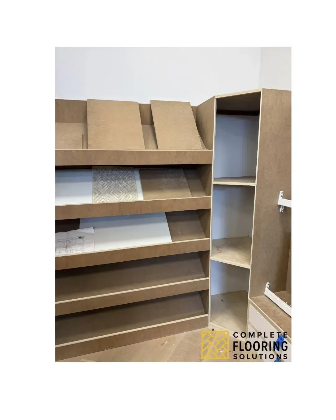 Cardboard shelving display with slanted slots and open cabinet, in a flooring showroom