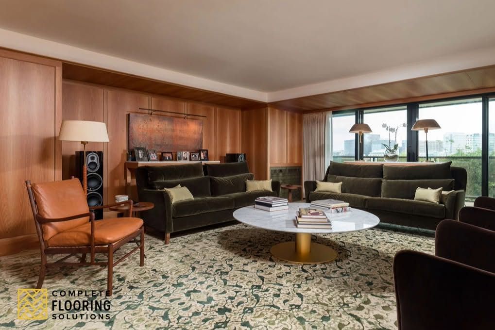 Mid-century living room with green sofas, patterned rug, wood paneling, and large windows.