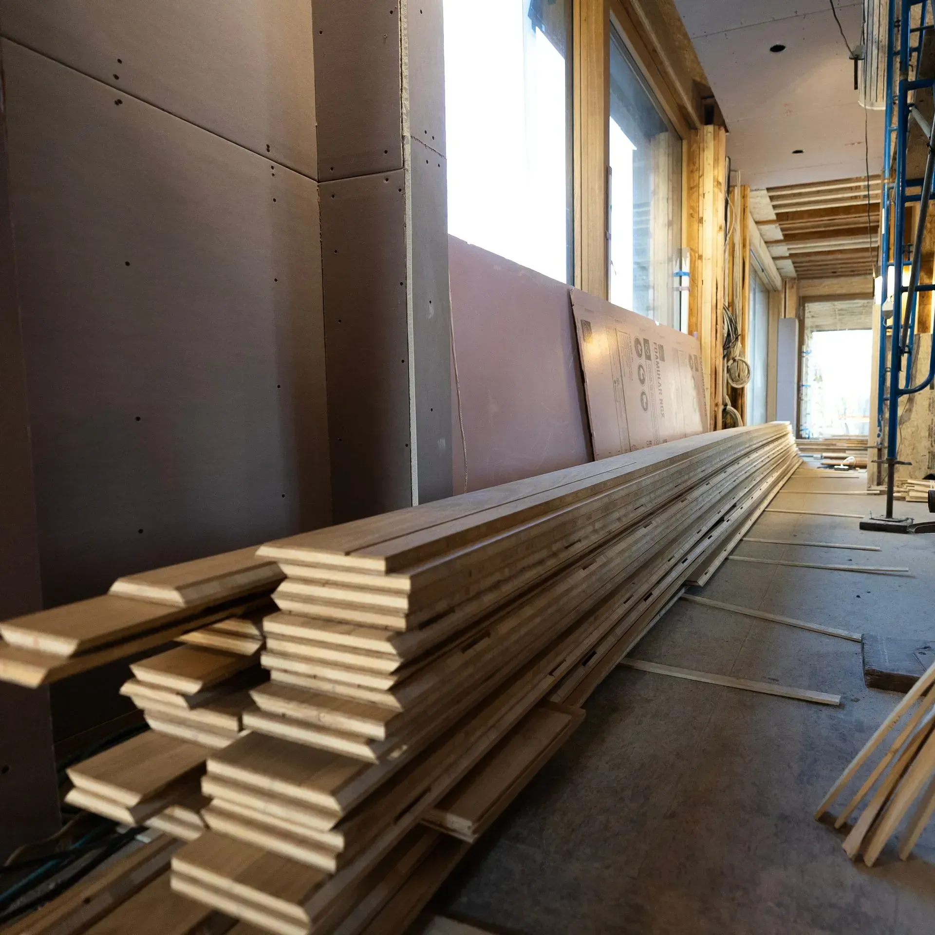 Stacked drywall boards in a narrow unfinished hallway at a construction site