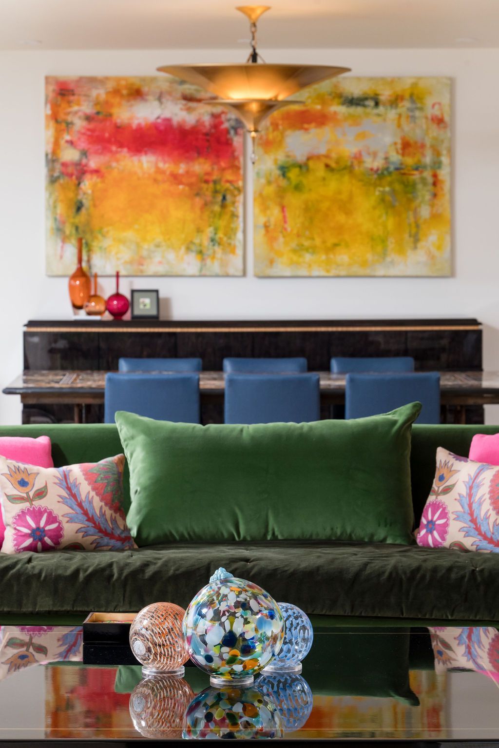 Modern living room with colorful abstract art, green sofa, blue chairs, and glass coffee table