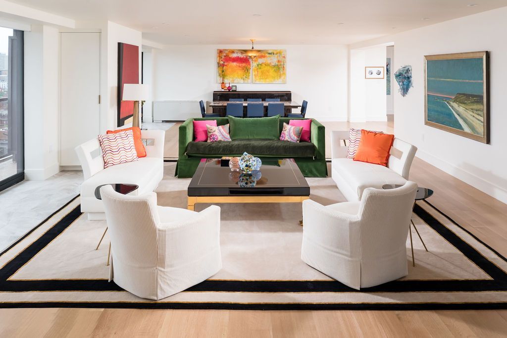 Bright modern living room with white chairs, black sofa, colorful pillows, and ocean art on the wall