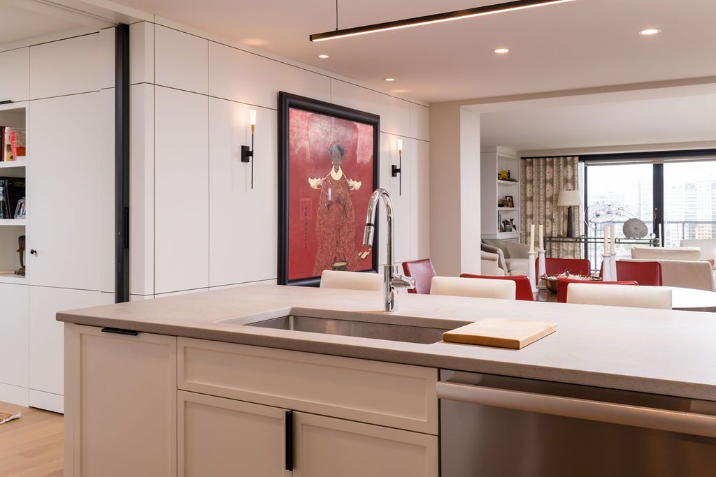 Modern white kitchen with a large island, sink, and recessed lighting, opening to a bright living room.