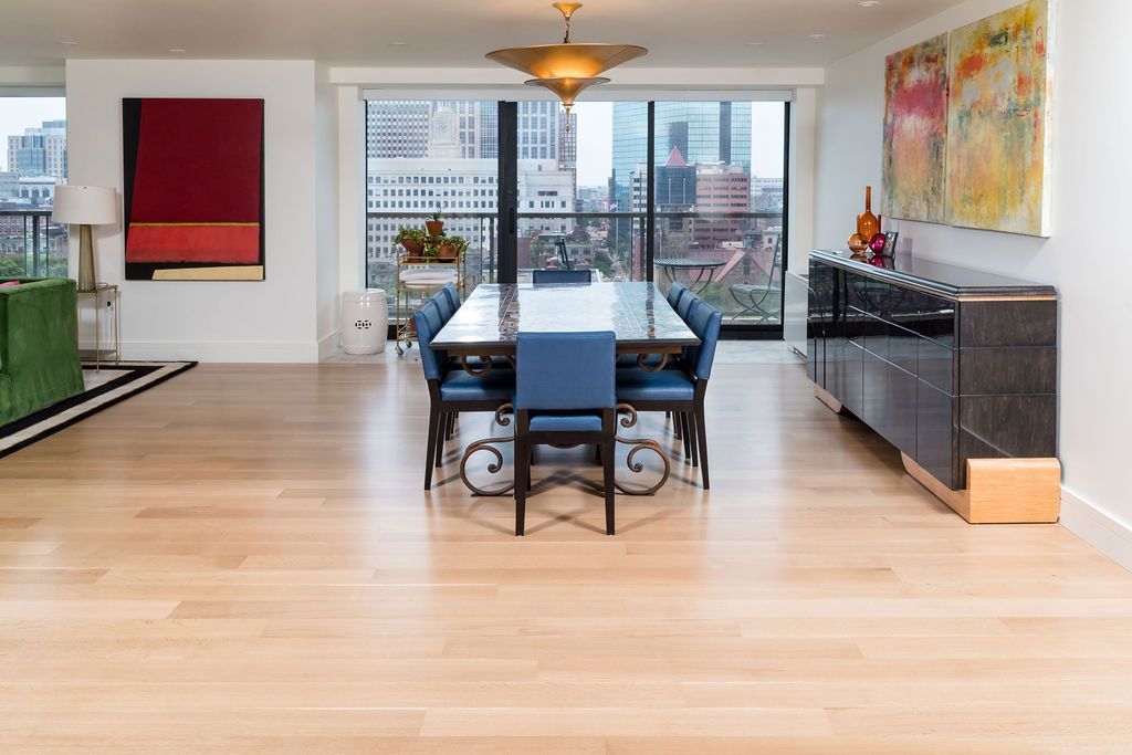 Modern dining room with long blue table, black chairs, hardwood floors, and city view windows