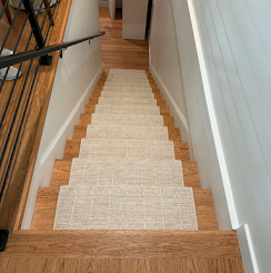 Carpeted wooden staircase descending between white walls with a black handrail on the left.