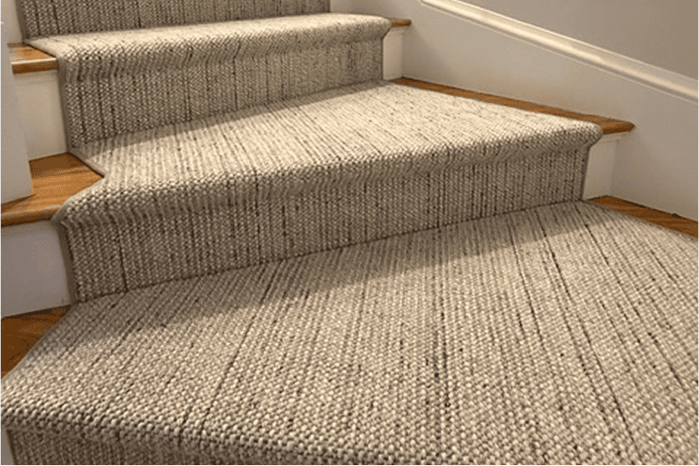 Carpeted staircase with beige runner and wooden handrails in a home interior