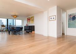 Spacious empty living and dining room with wood floors, black table, and city view through windows