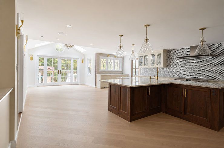 Bright modern kitchen with dark island, marble backsplash, and open living area with large windows
