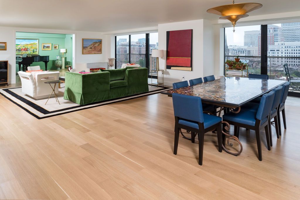 Bright open-plan living and dining room with green sofa, blue chairs, and city views.