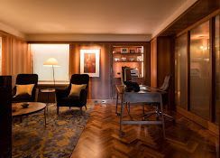 Elegant living room with wooden floors, patterned rug, chairs, lamp, and large window blinds.