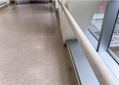 Indoor corridor with terrazzo floor and white railing beside large windows.