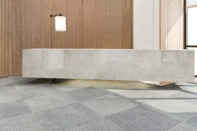 Modern minimalist lobby with a long stone bench, wood slat wall, and gray patterned floor.