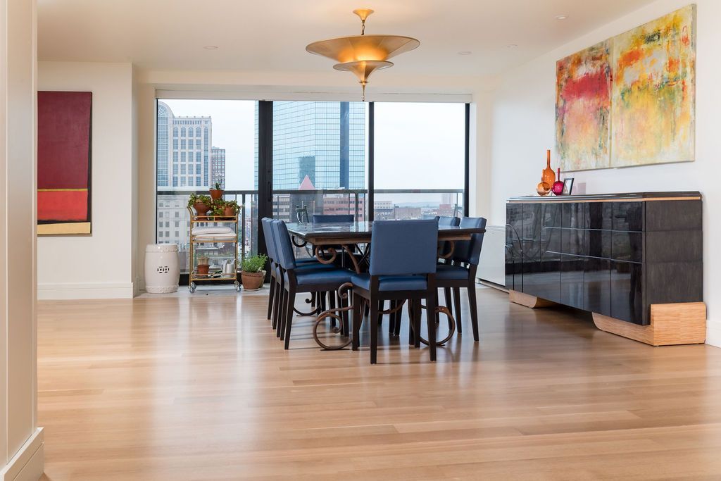 Bright dining room with table, chairs, large windows, wood floors, and a sideboard with colorful wall art.