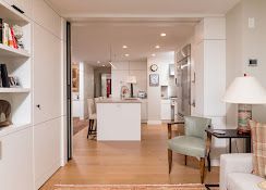 Bright, modern open-plan living space with white cabinetry, wood floors, and a small seating area near the kitchen.