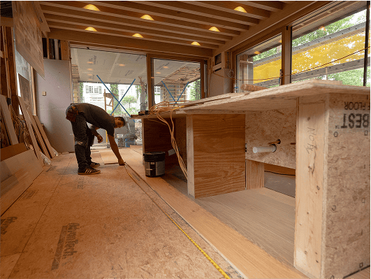 Worker installing wood framing inside a partially finished interior room under construction.