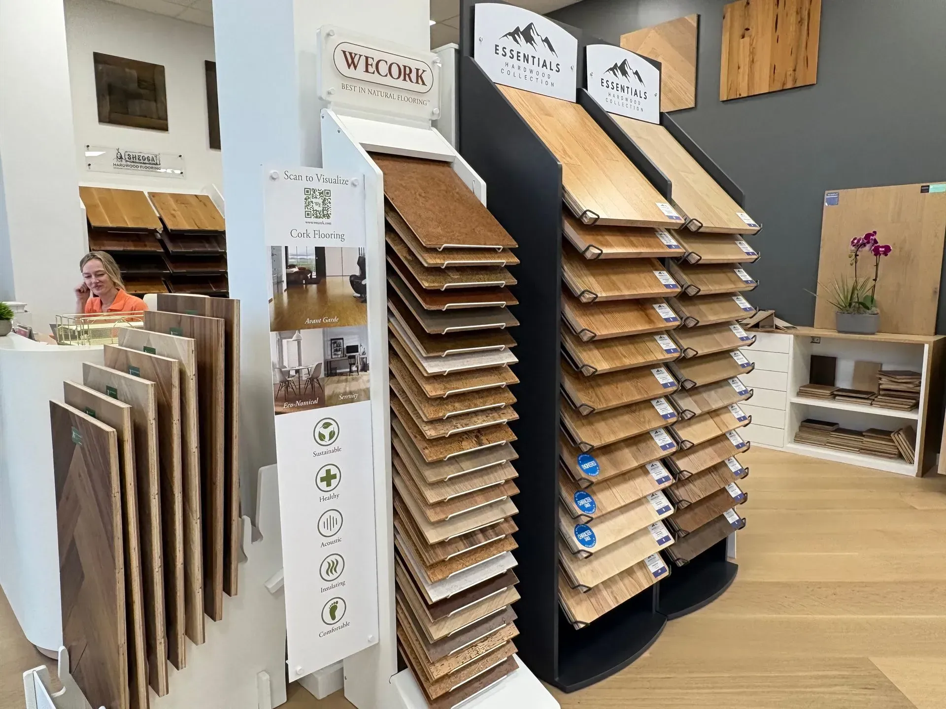 Showroom display of wood flooring samples on racks with sample boards and a light wood floor in the background