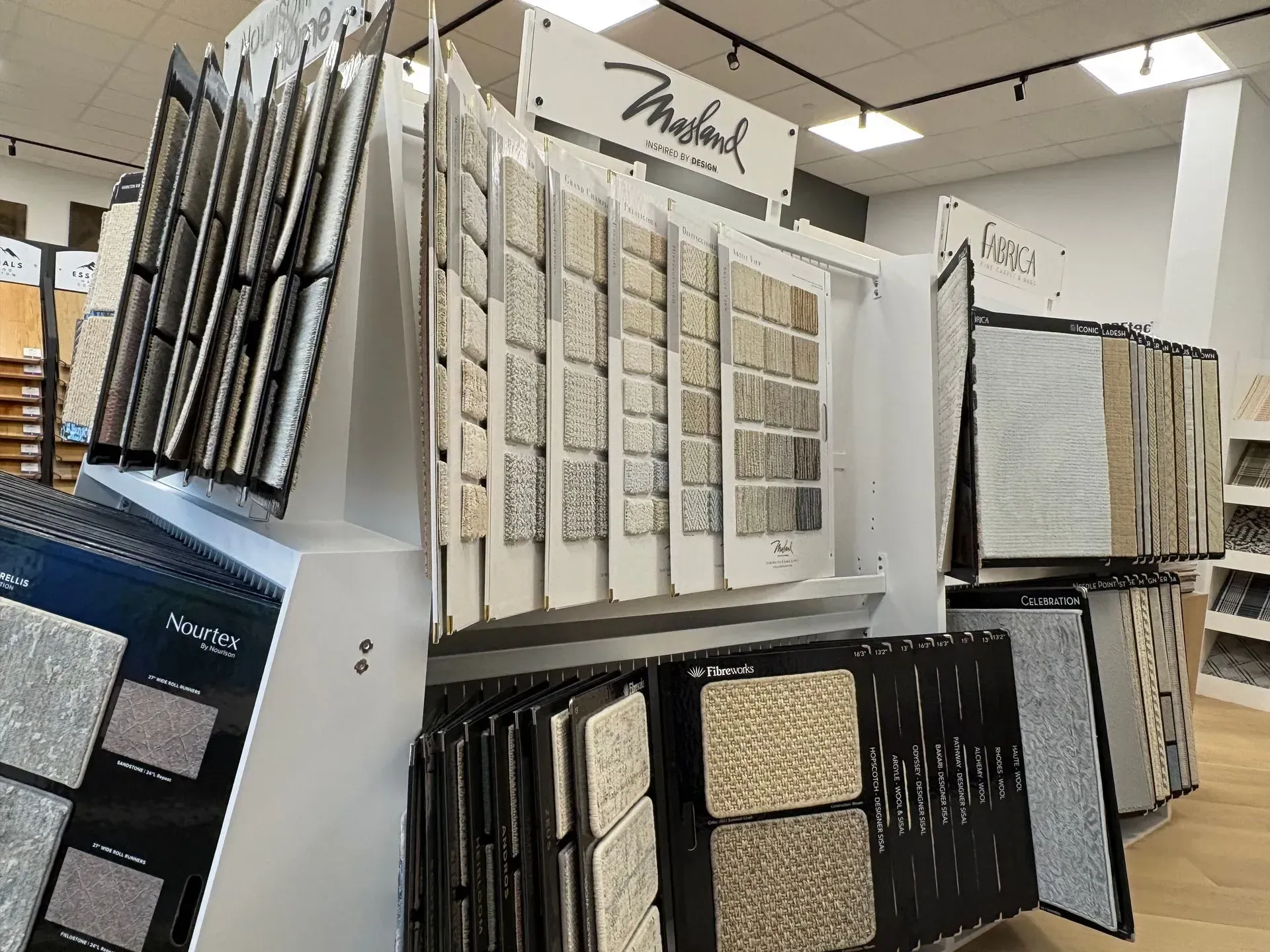 Fabric and wallpaper sample display racks in a showroom, with neutral and patterned swatches on shelves.
