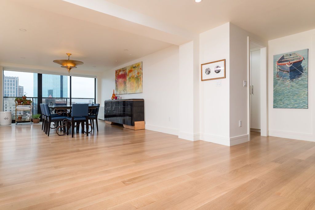 Spacious empty living and dining room with hardwood floors, city-view windows, and colorful wall art.