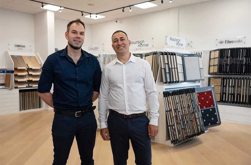 Two men standing in a showroom with display racks of flooring samples and wood panels