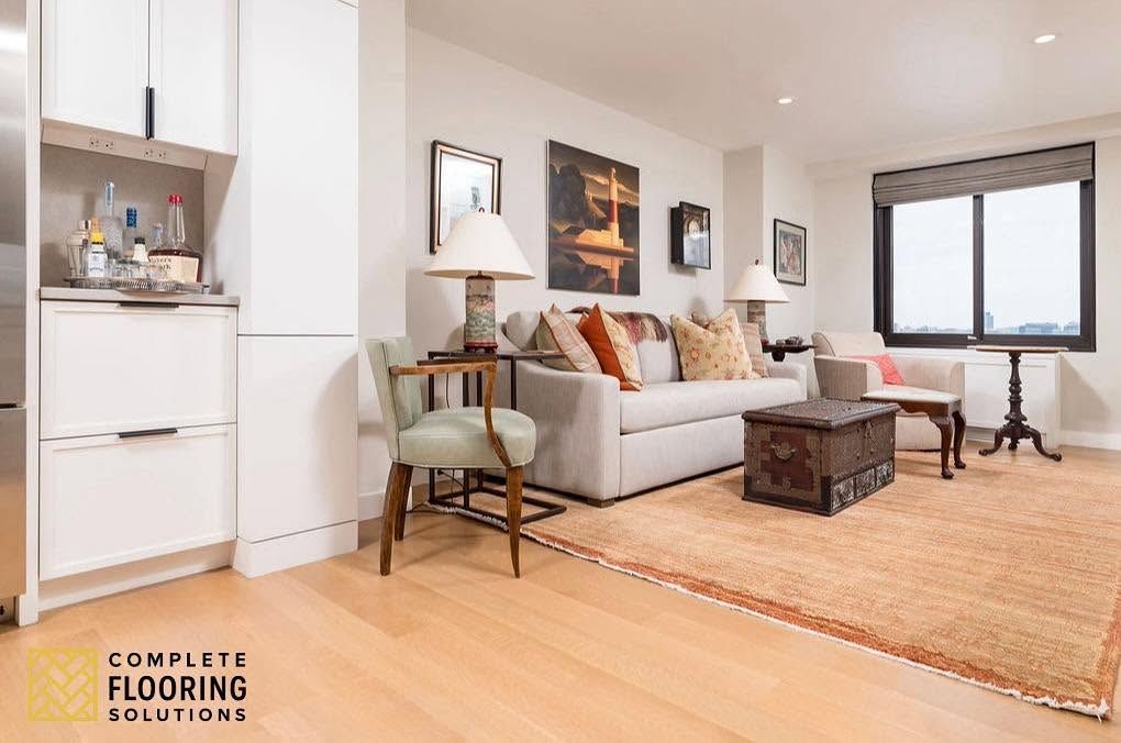 Bright minimalist living room with gray sofa, wood floor, rug, coffee table, and large windows