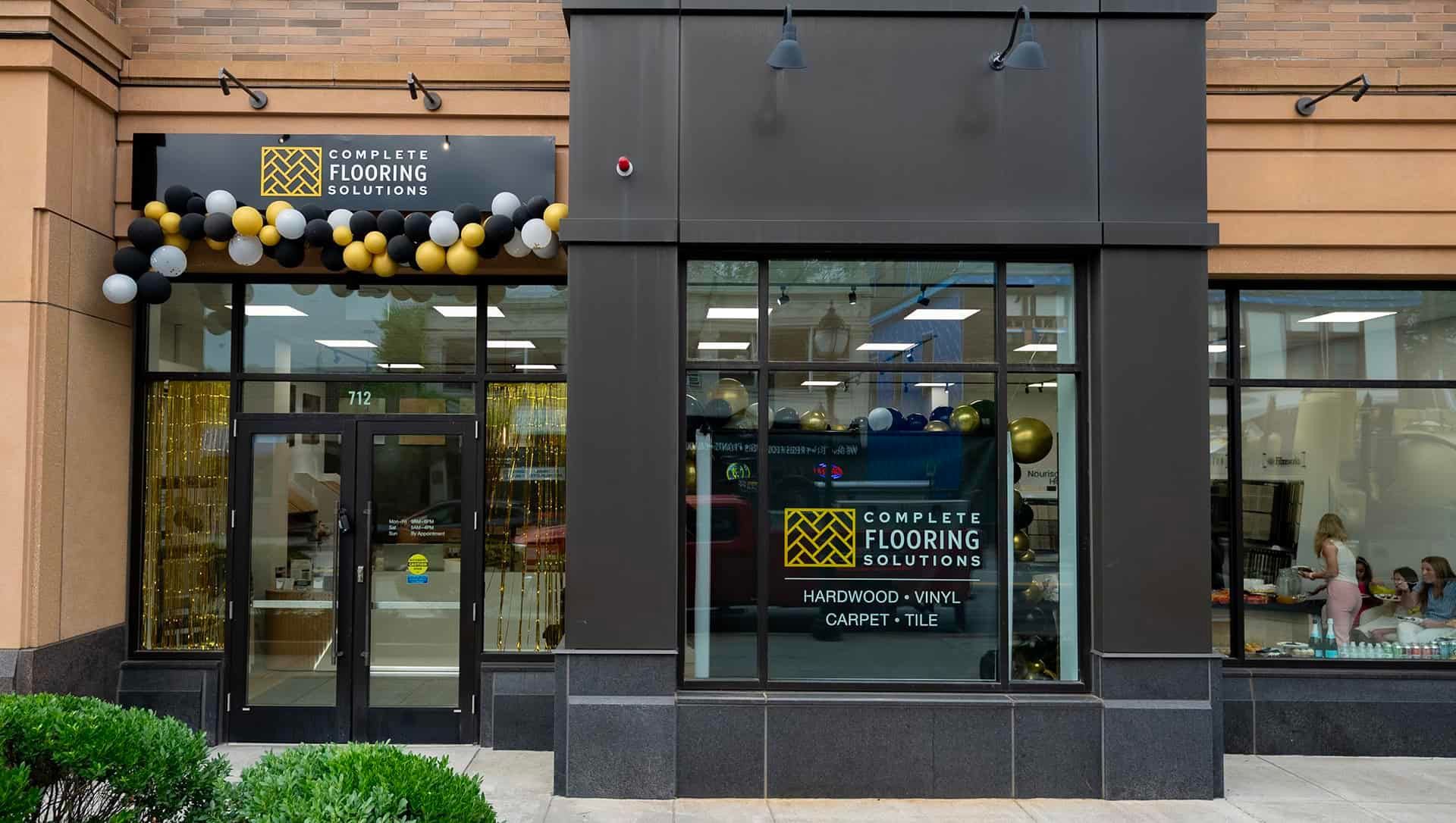 Storefront with dark facade, glass door, and large windows under a row of hanging lights