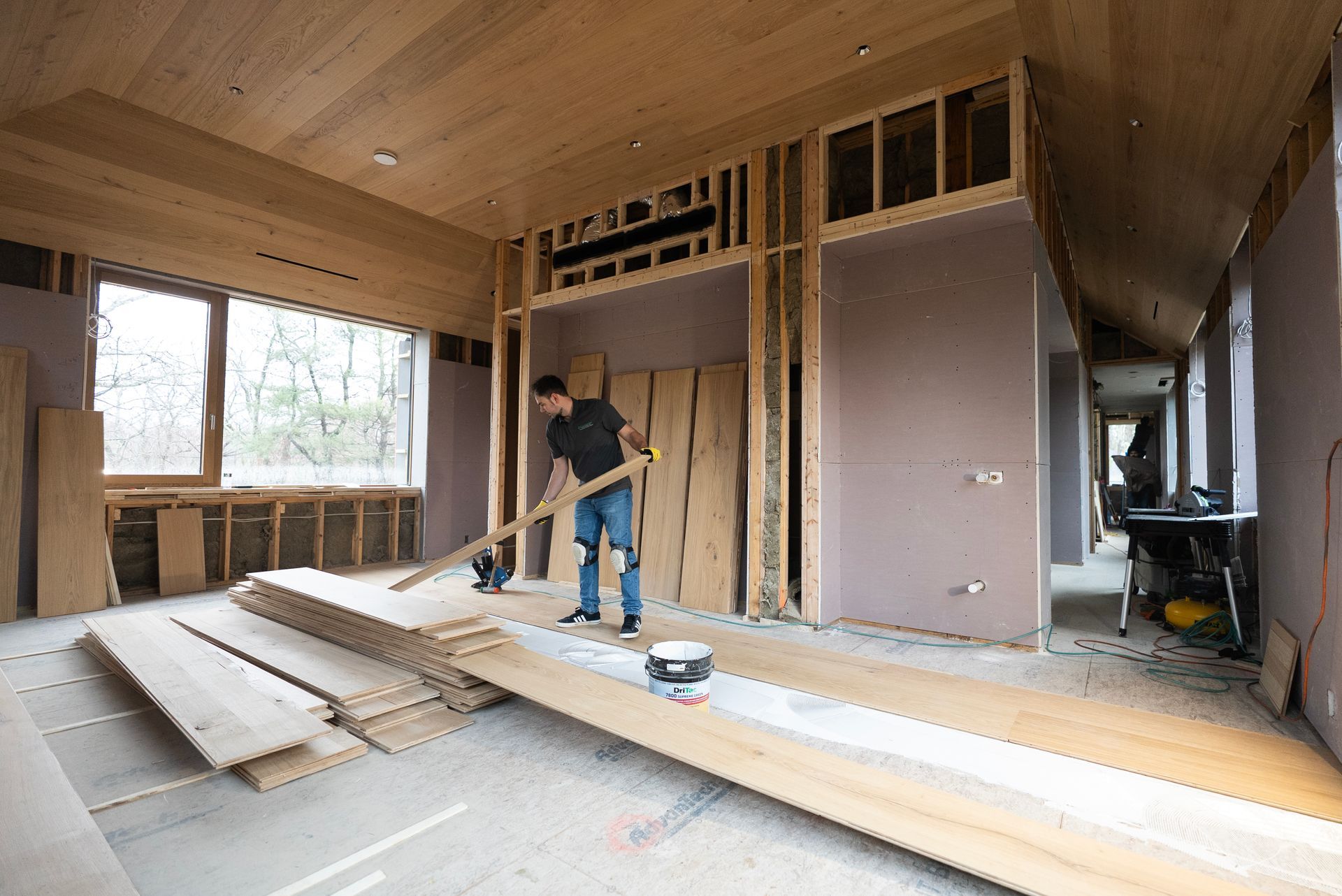 Worker framing a room under construction with wood beams, insulation, and tools scattered on the floor.