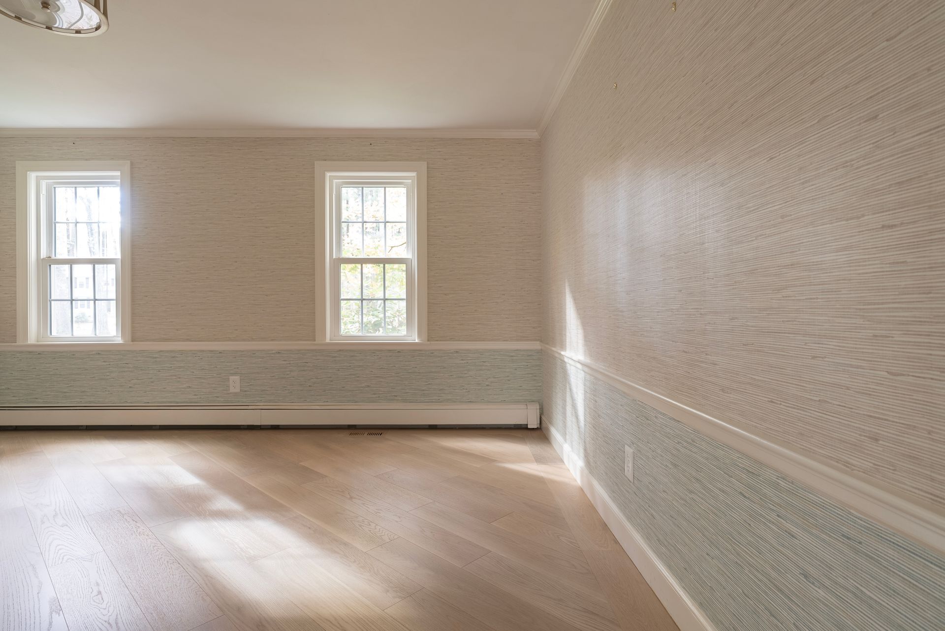 Empty beige room with hardwood floors, two windows, and white trim.