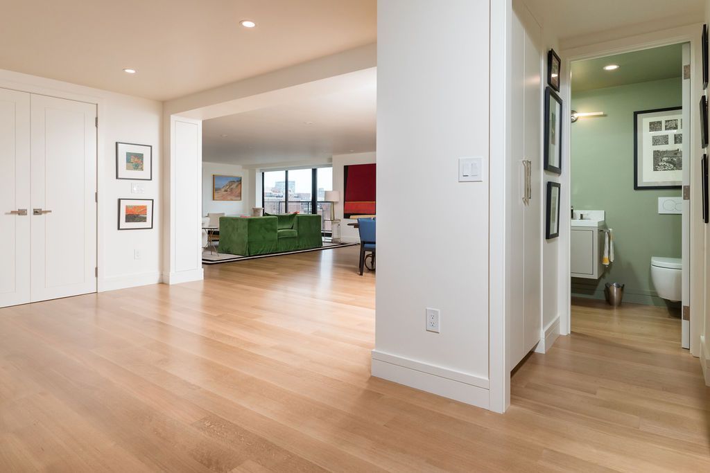 Bright open living room with wood floors, white walls, and a hallway leading to a small bathroom.
