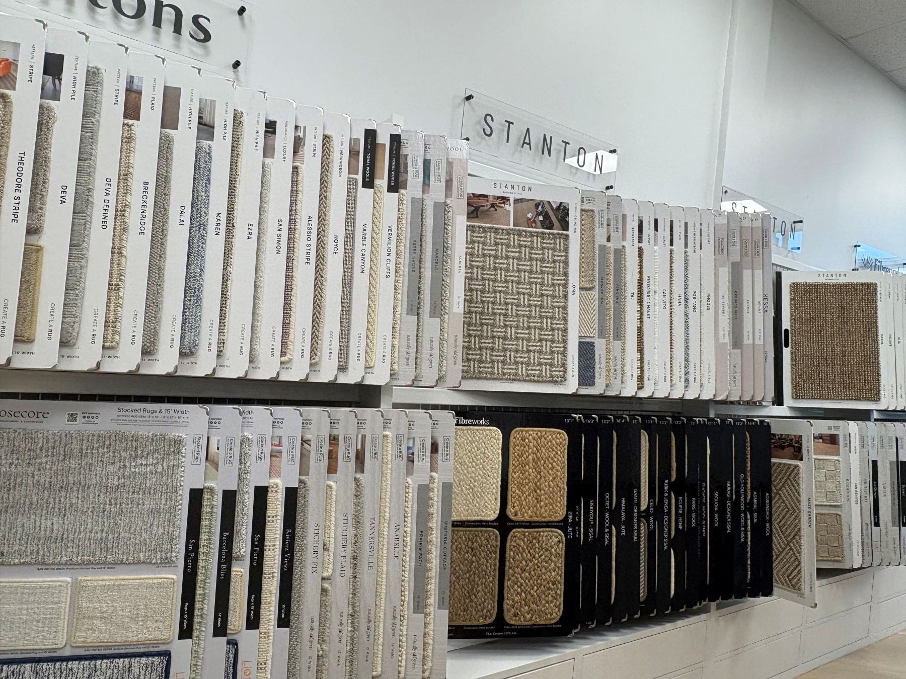 Display of patterned tile samples on wall racks in a showroom, in neutral tones and black accents