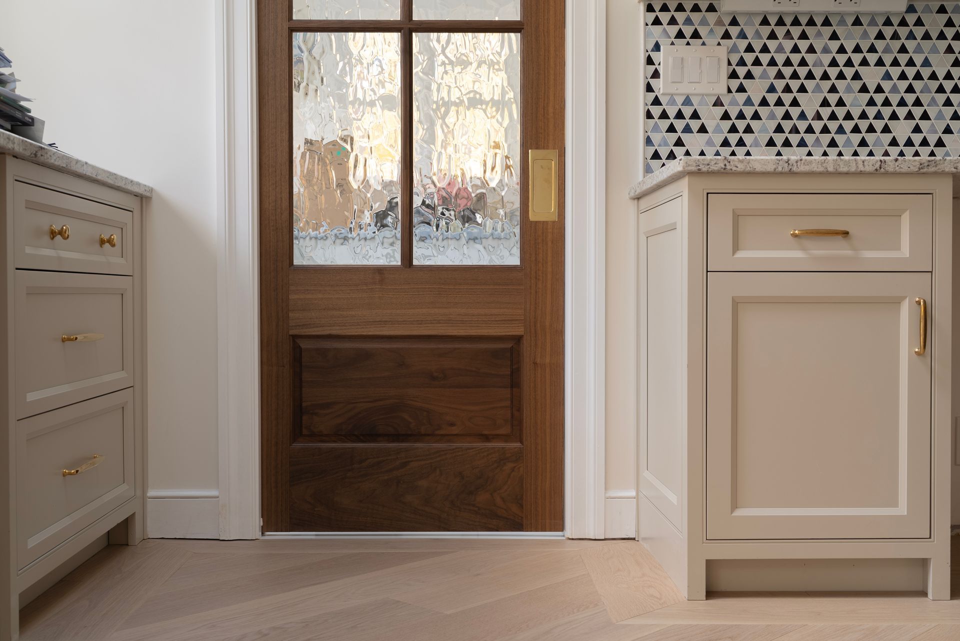 Elegant entryway with a wood-and-glass door, white dresser, and beige cabinet with black-and-white tile backsplash.