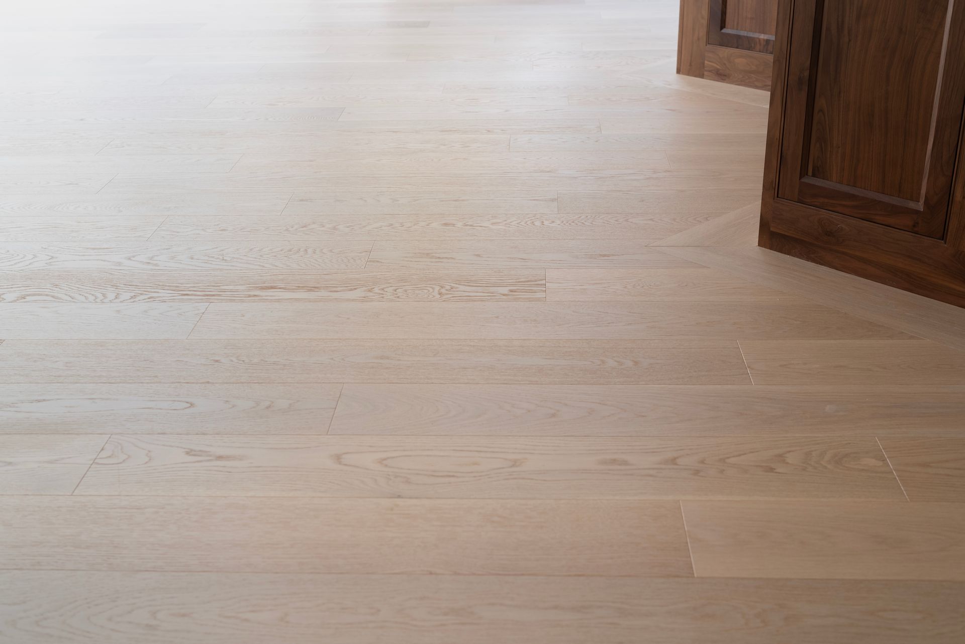 Light wood floor with part of a dark wooden cabinet on the right side