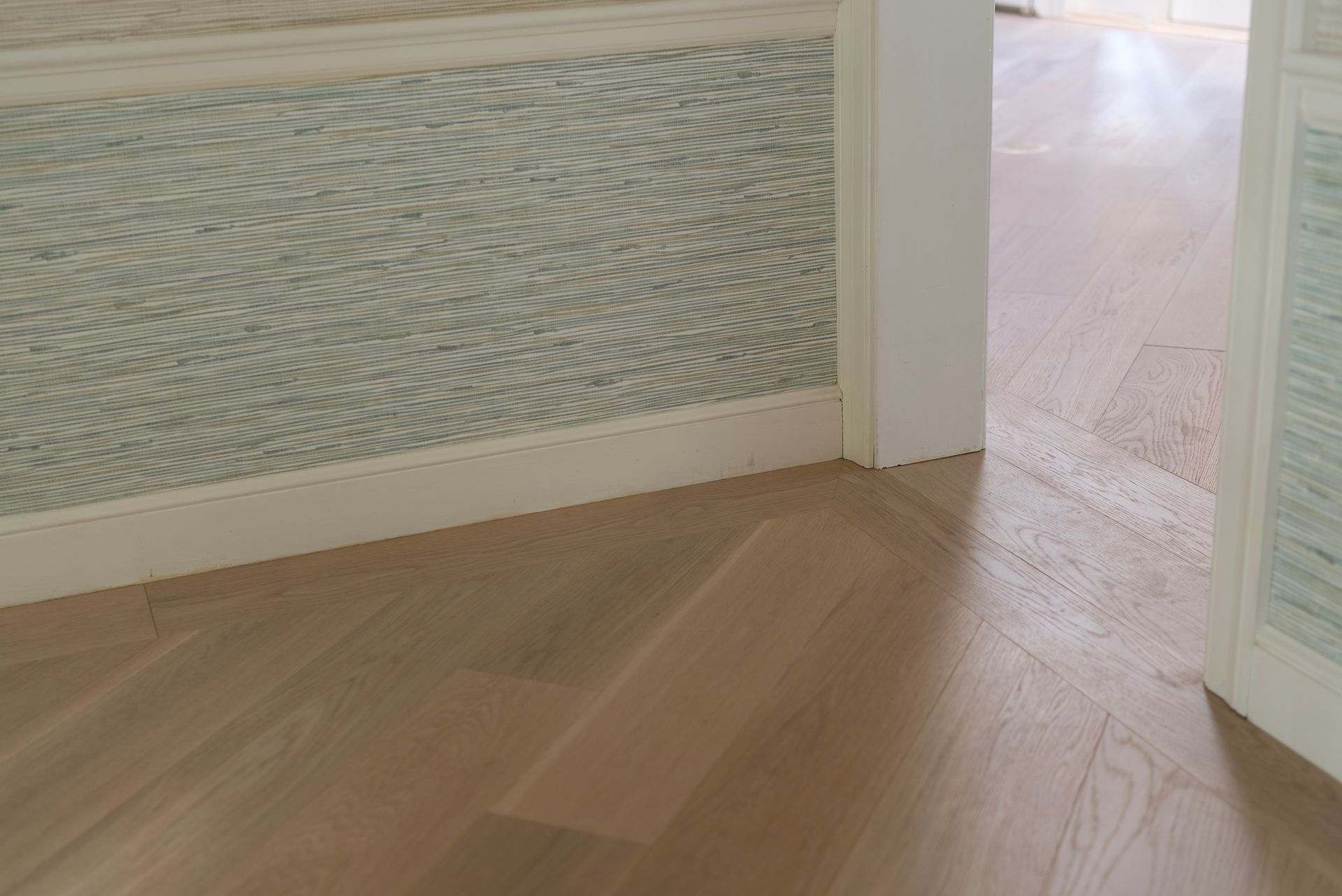 Light wood floor and patterned wall paneling in a hallway with an open doorway to a bright room