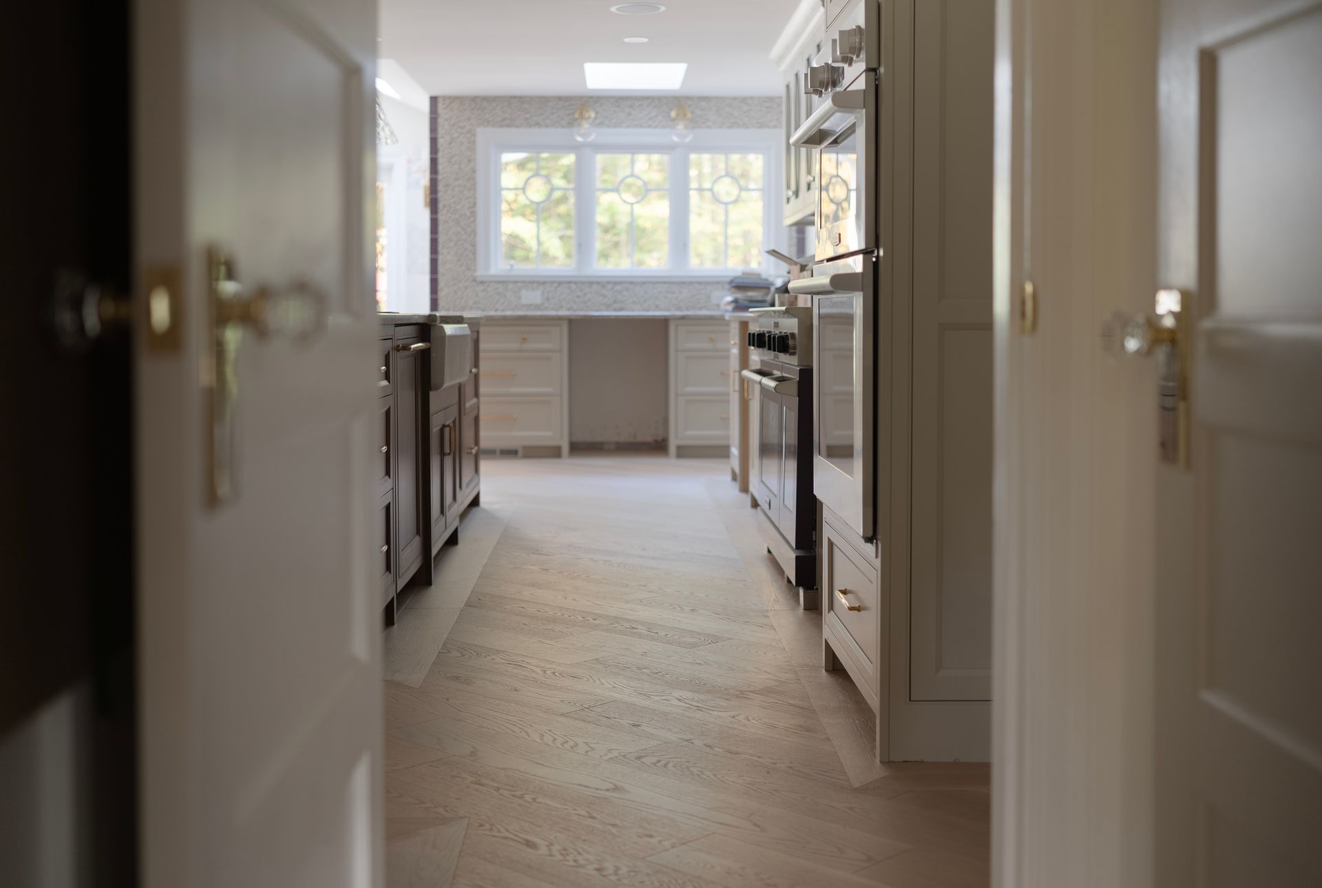 Bright modern kitchen hallway with white cabinets and a large window at the end