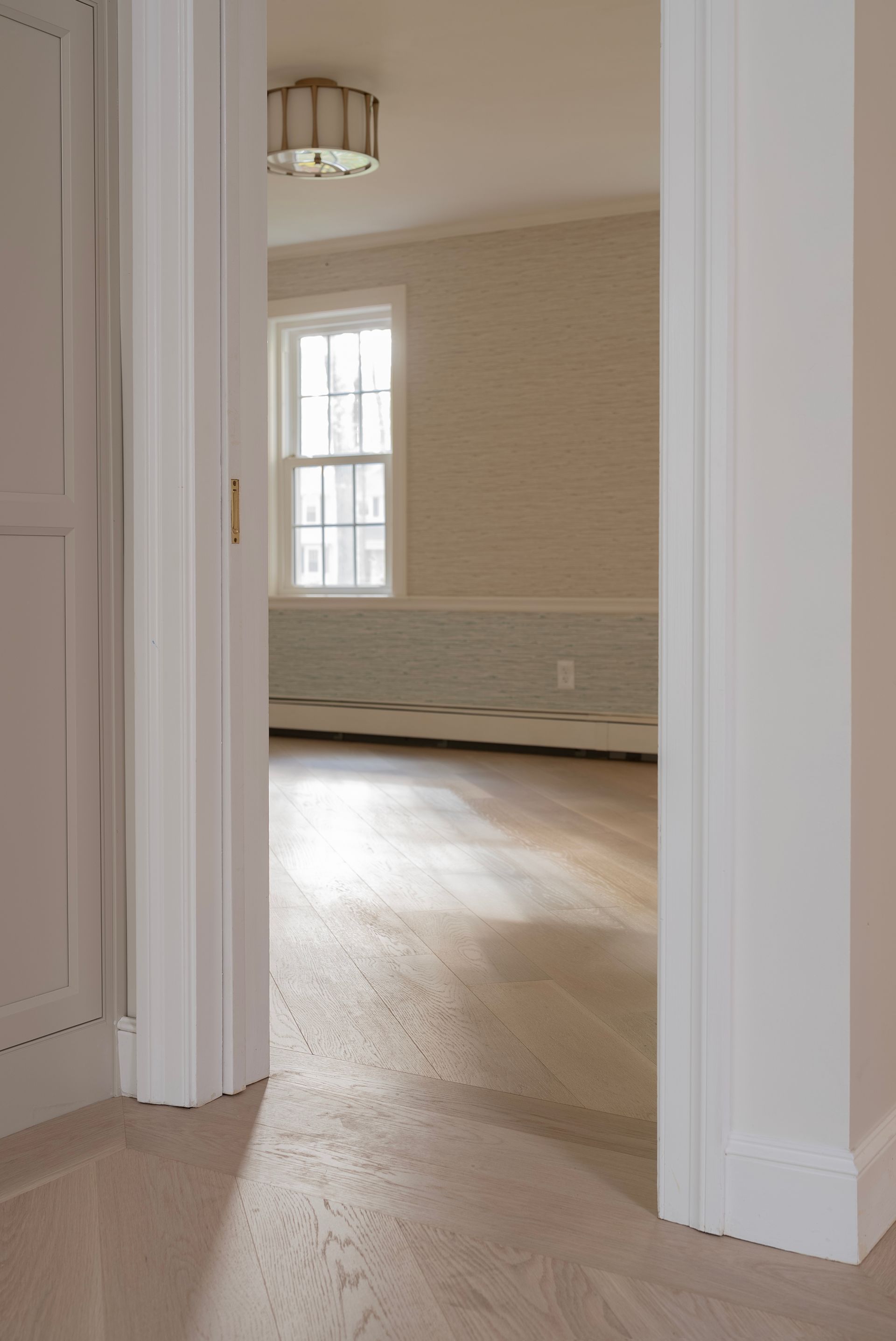 Empty beige room viewed through a doorway, with white trim, wood floor, and a window