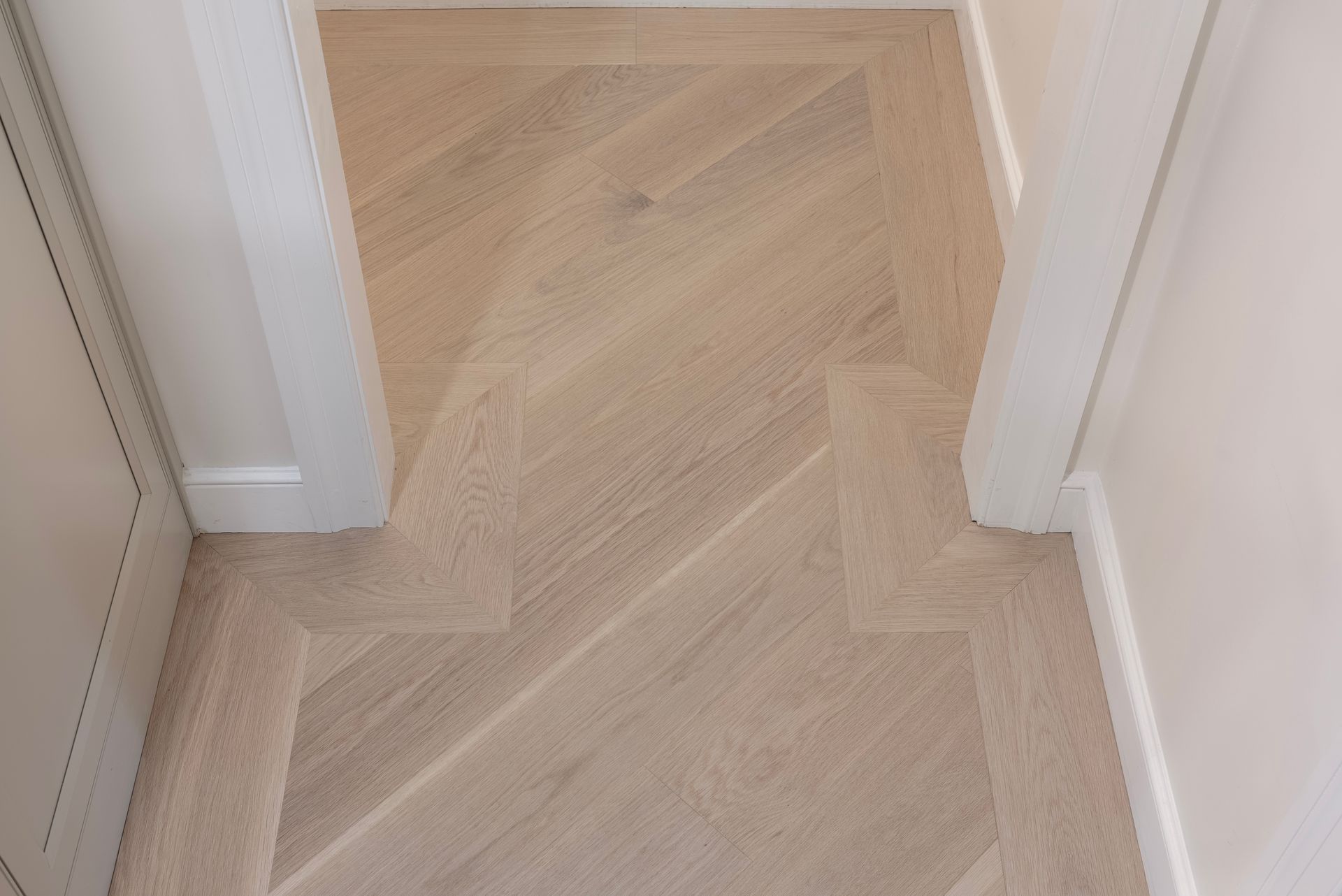 Light wood herringbone flooring in a narrow hallway between white walls and doorways