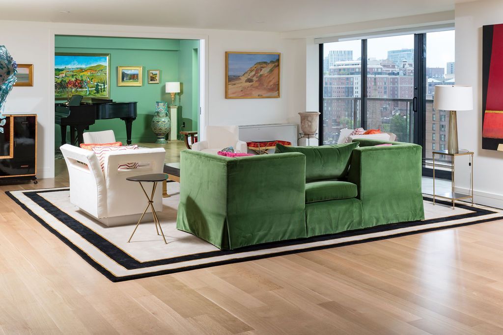 Bright living room with green sofas, white chairs, artwork, and large windows overlooking a city view