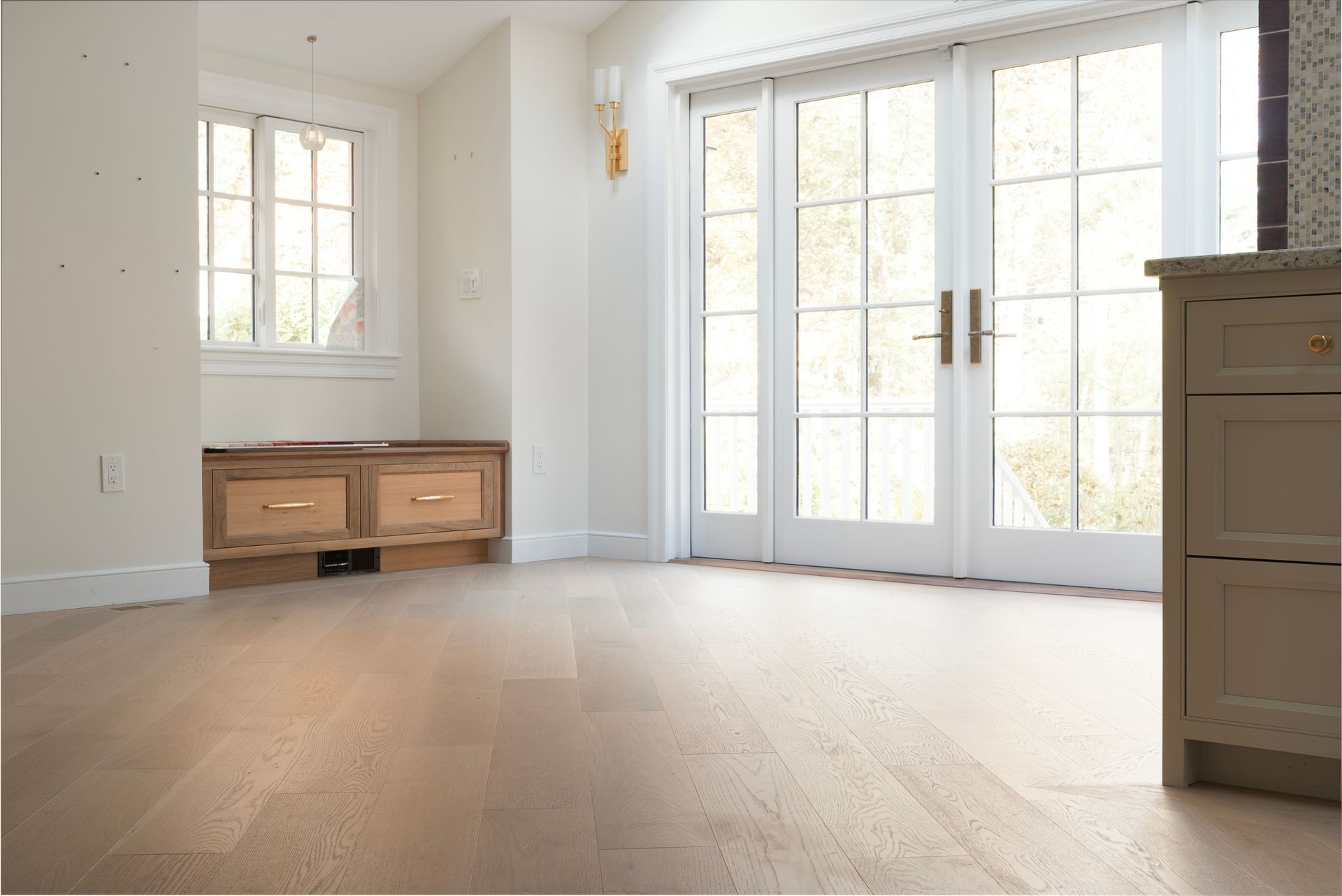 Bright empty room with hardwood floors, French doors, small window, and a wooden cabinet