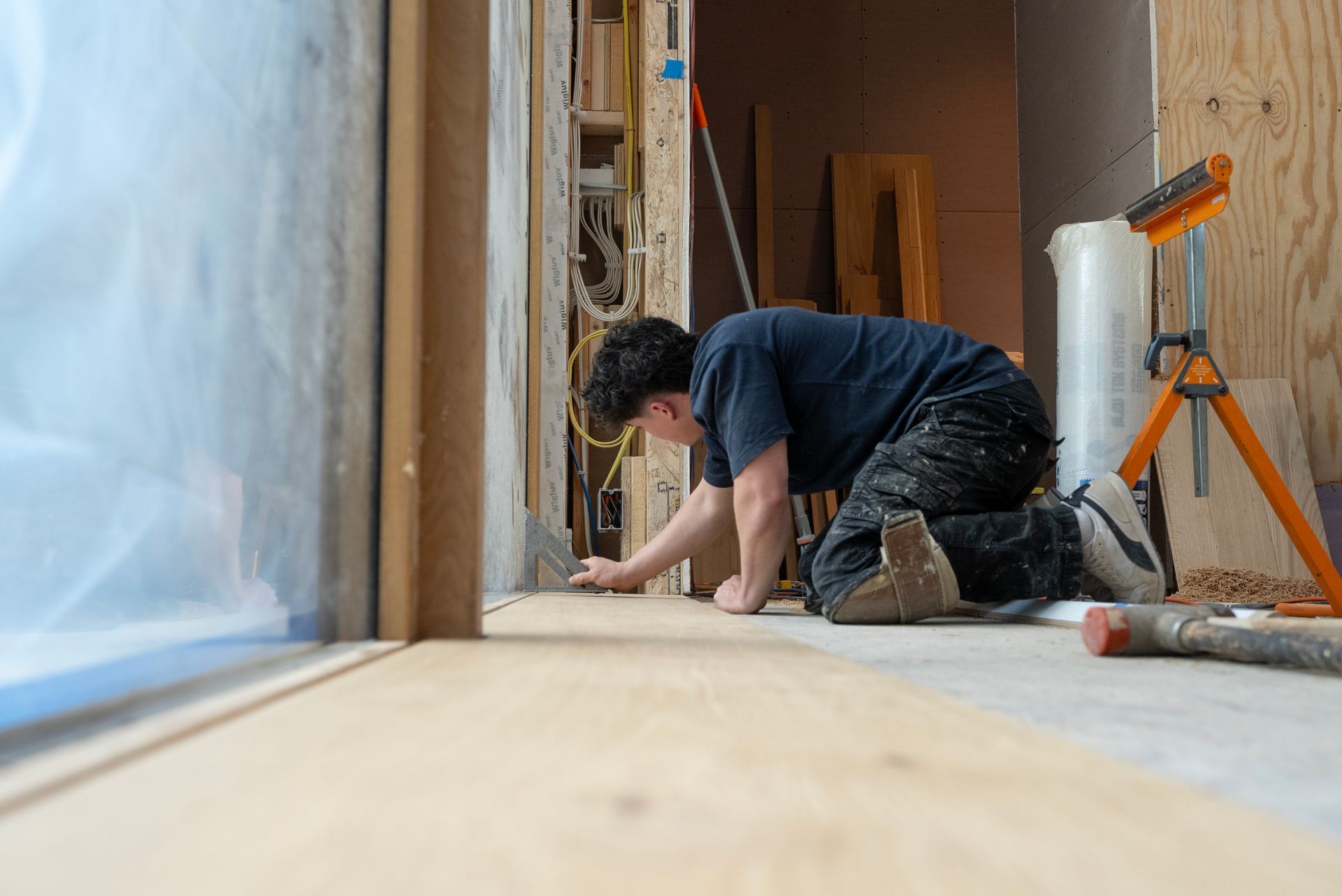 Person kneeling on a floor, measuring and working on wood during a home renovation.