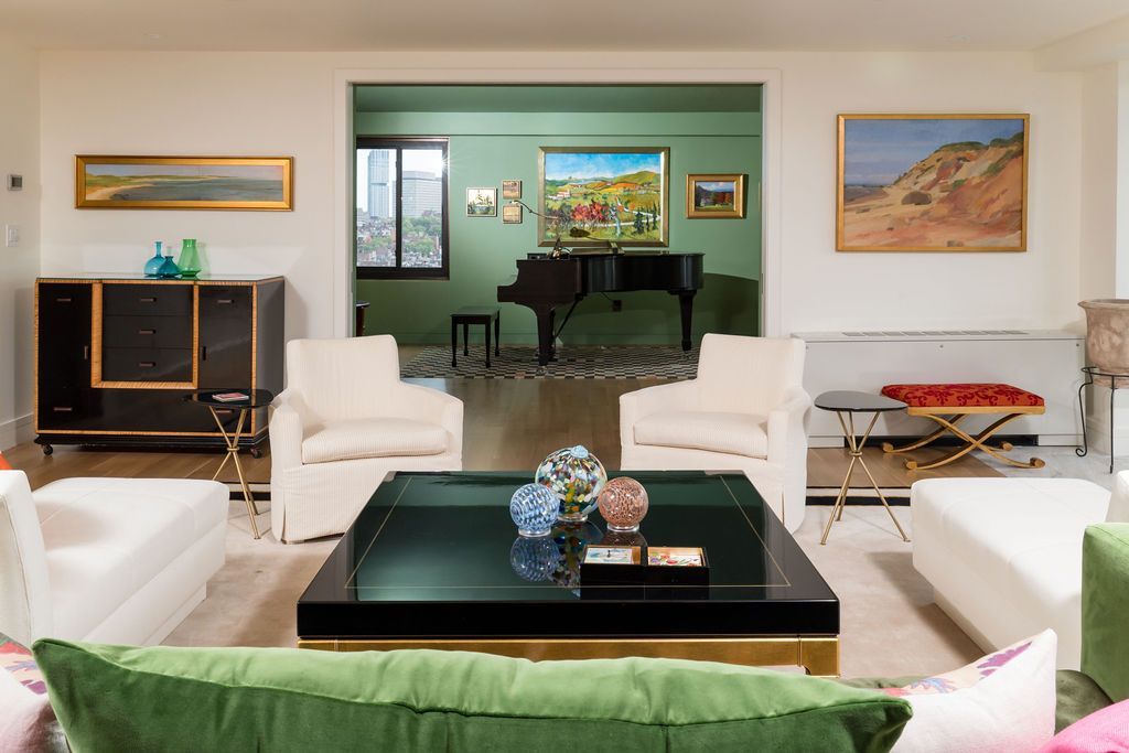 Bright modern living room with white sofas, black coffee table, and a view into a dining area beyond.