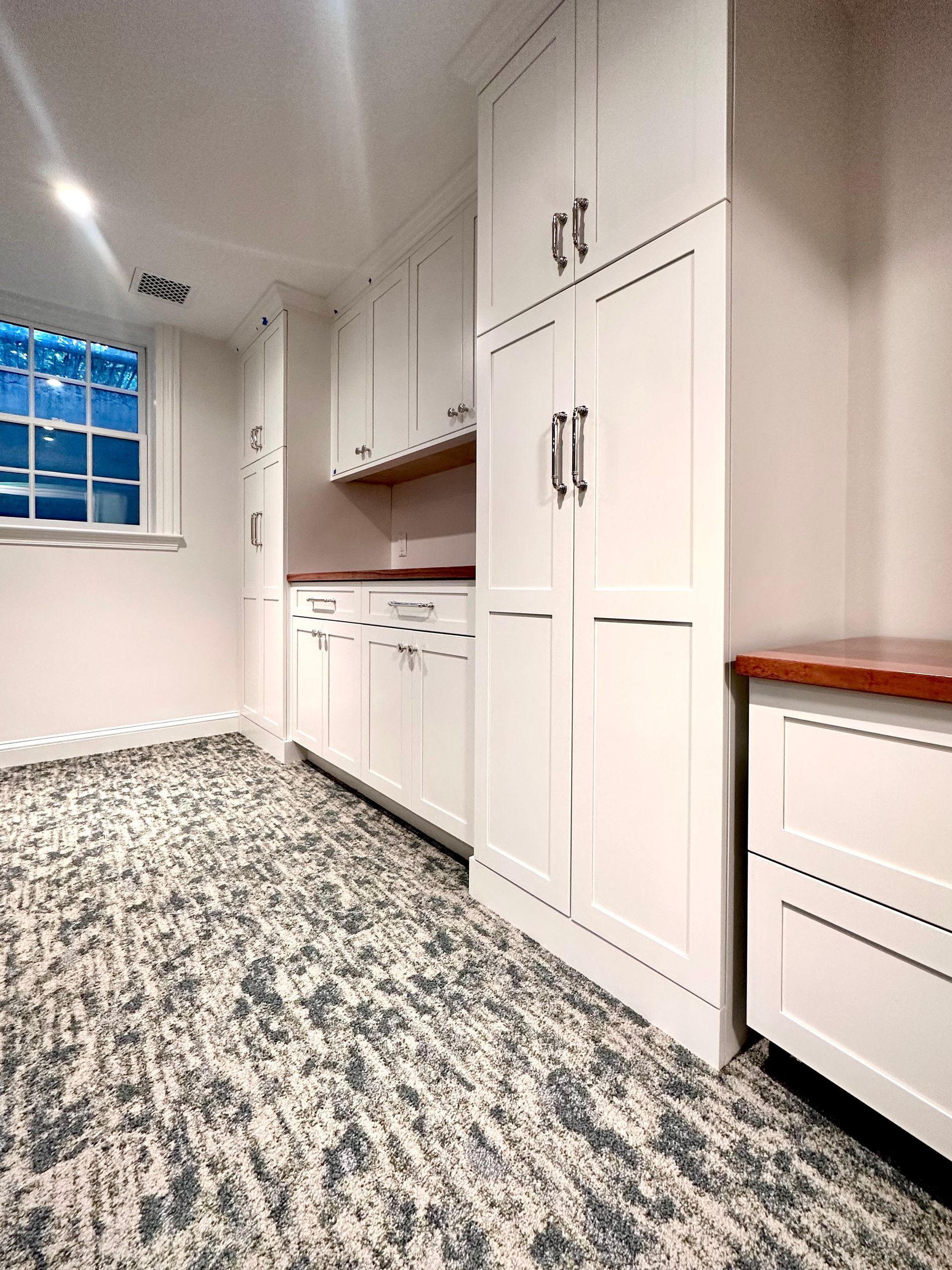 Bright laundry room with white cabinets, speckled floor, window, and wood countertop.