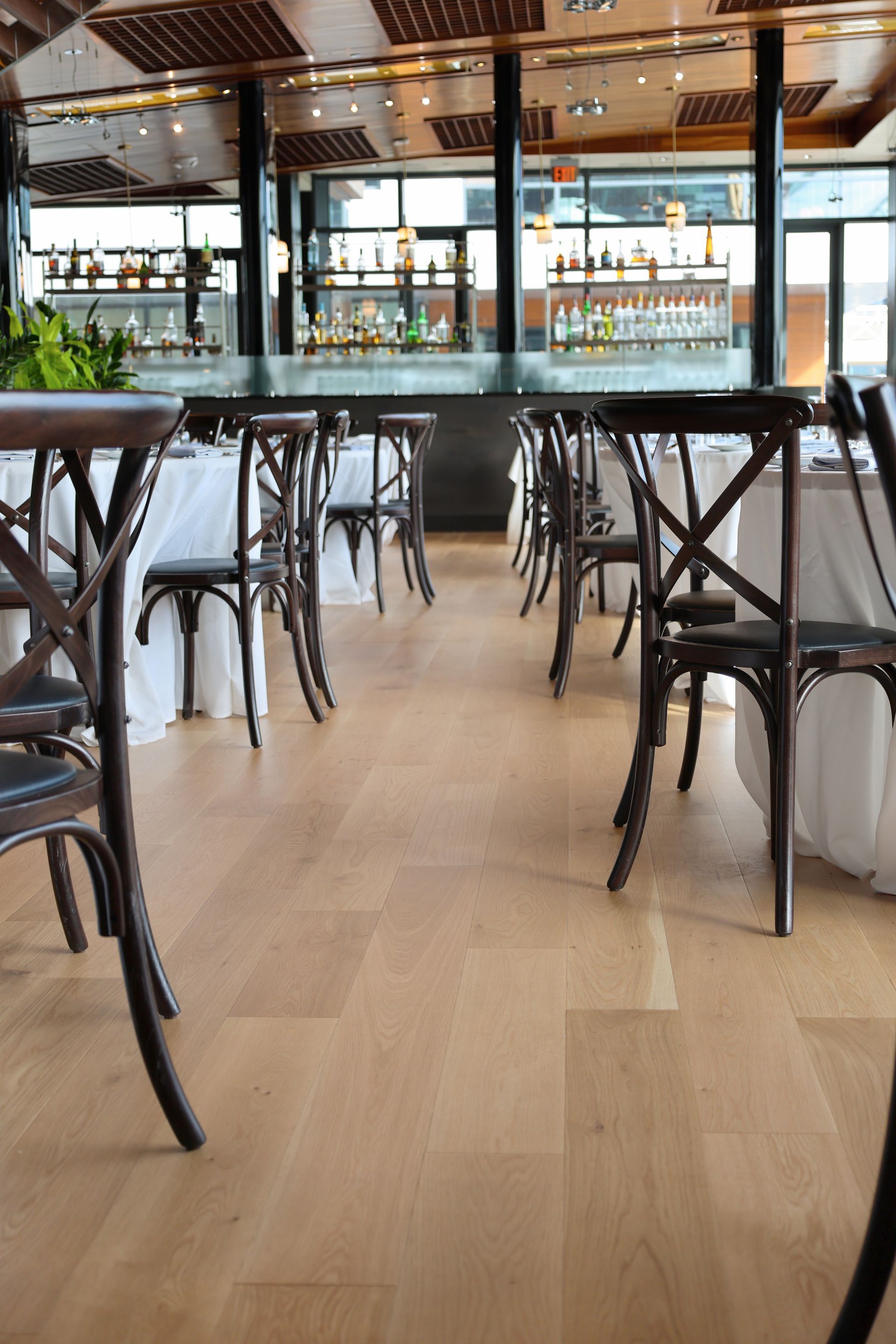 Empty modern bar with high stools and a wooden floor, lit by large windows.
