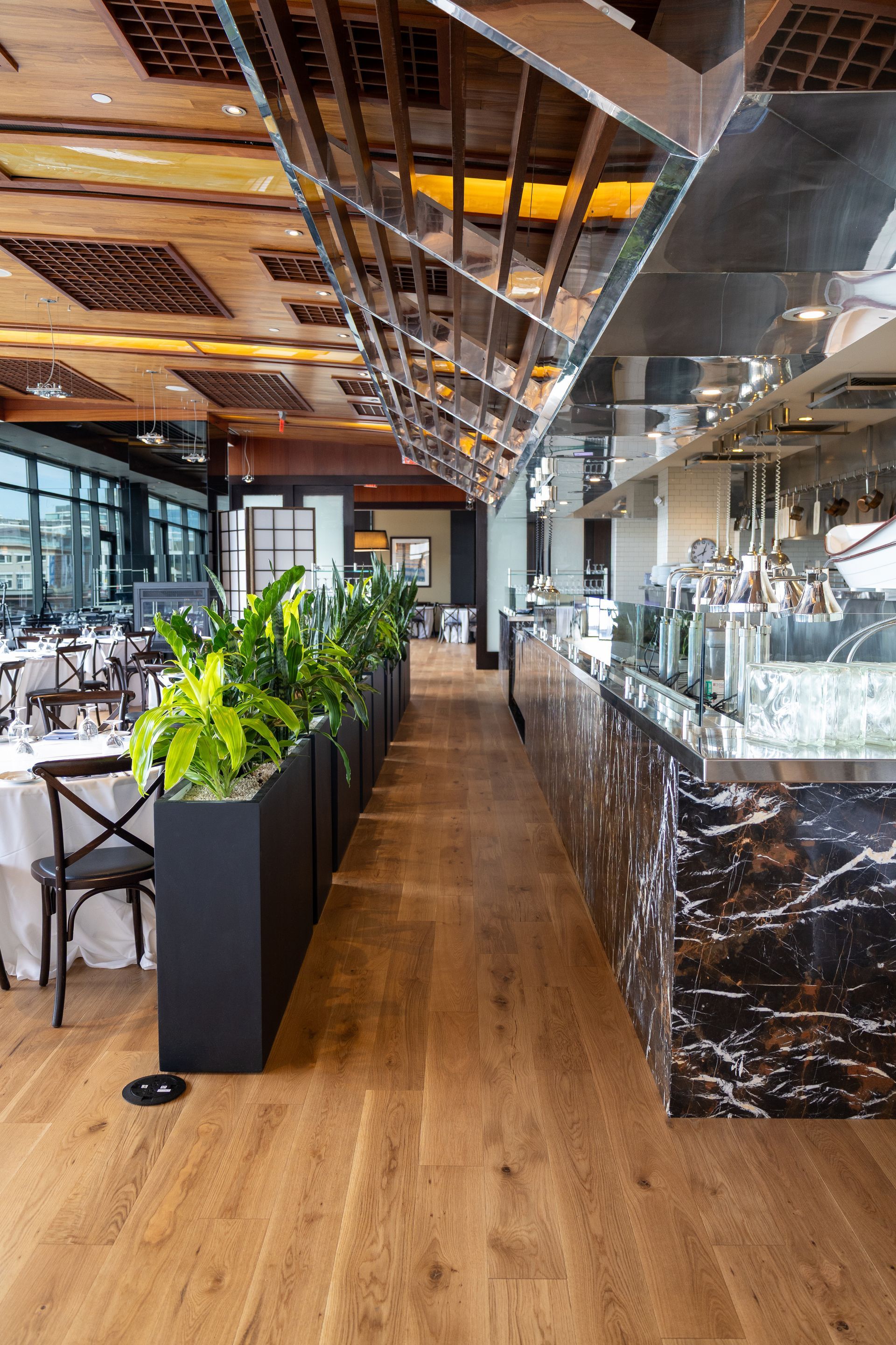 Modern restaurant interior with wooden floor, marble bar, and mirrored ceiling reflecting tables and plants
