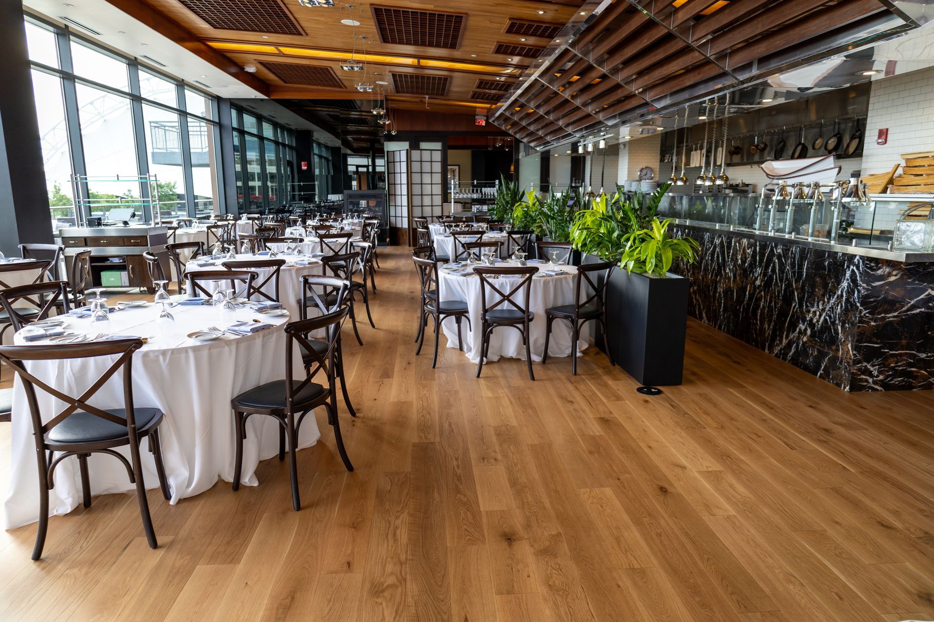 Modern restaurant interior with white tablecloth tables, wooden chairs, and a bar under a wood ceiling