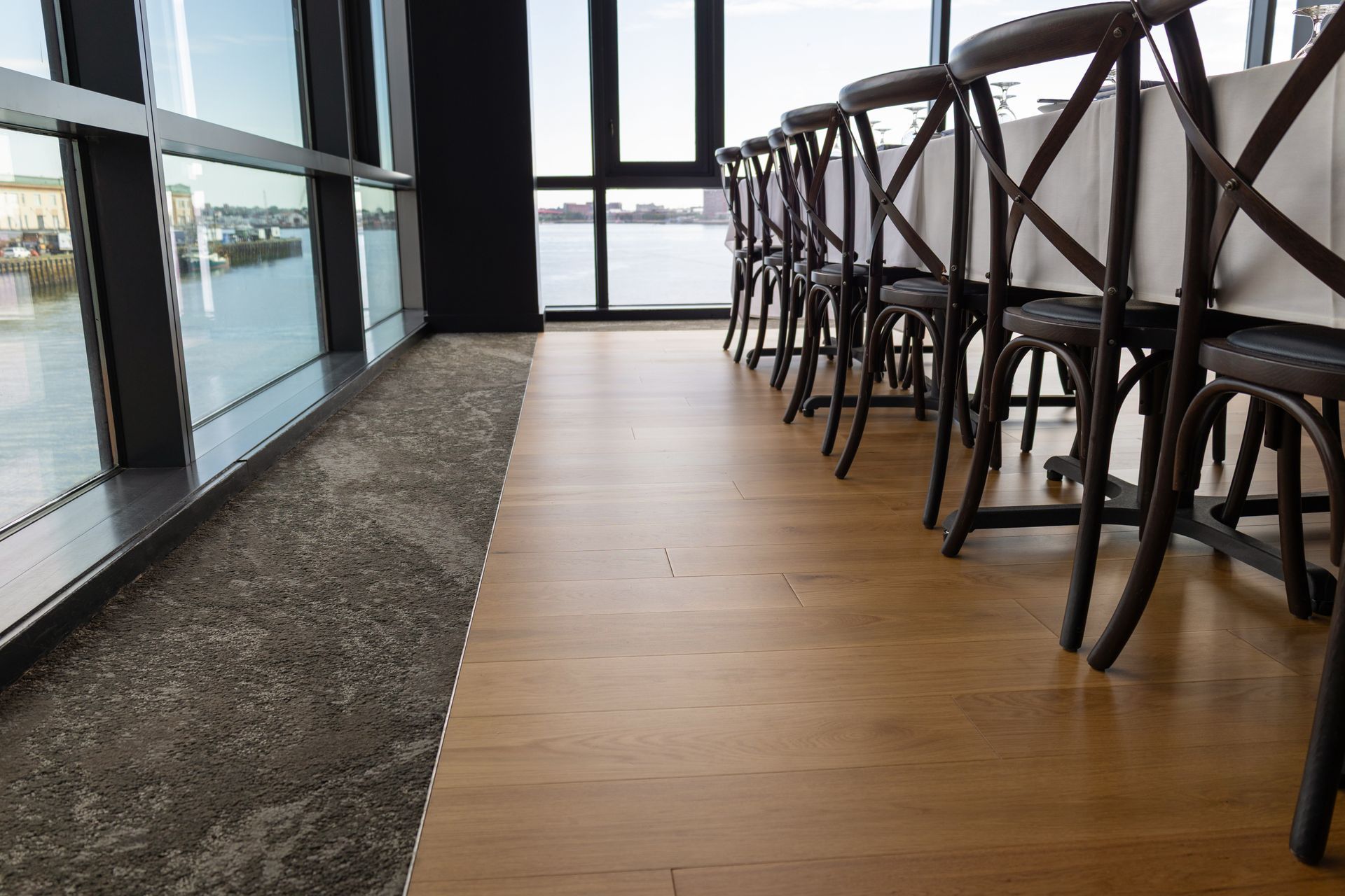 Empty modern cafe with wooden floor, chairs upside down on tables, and large windows overlooking the water.