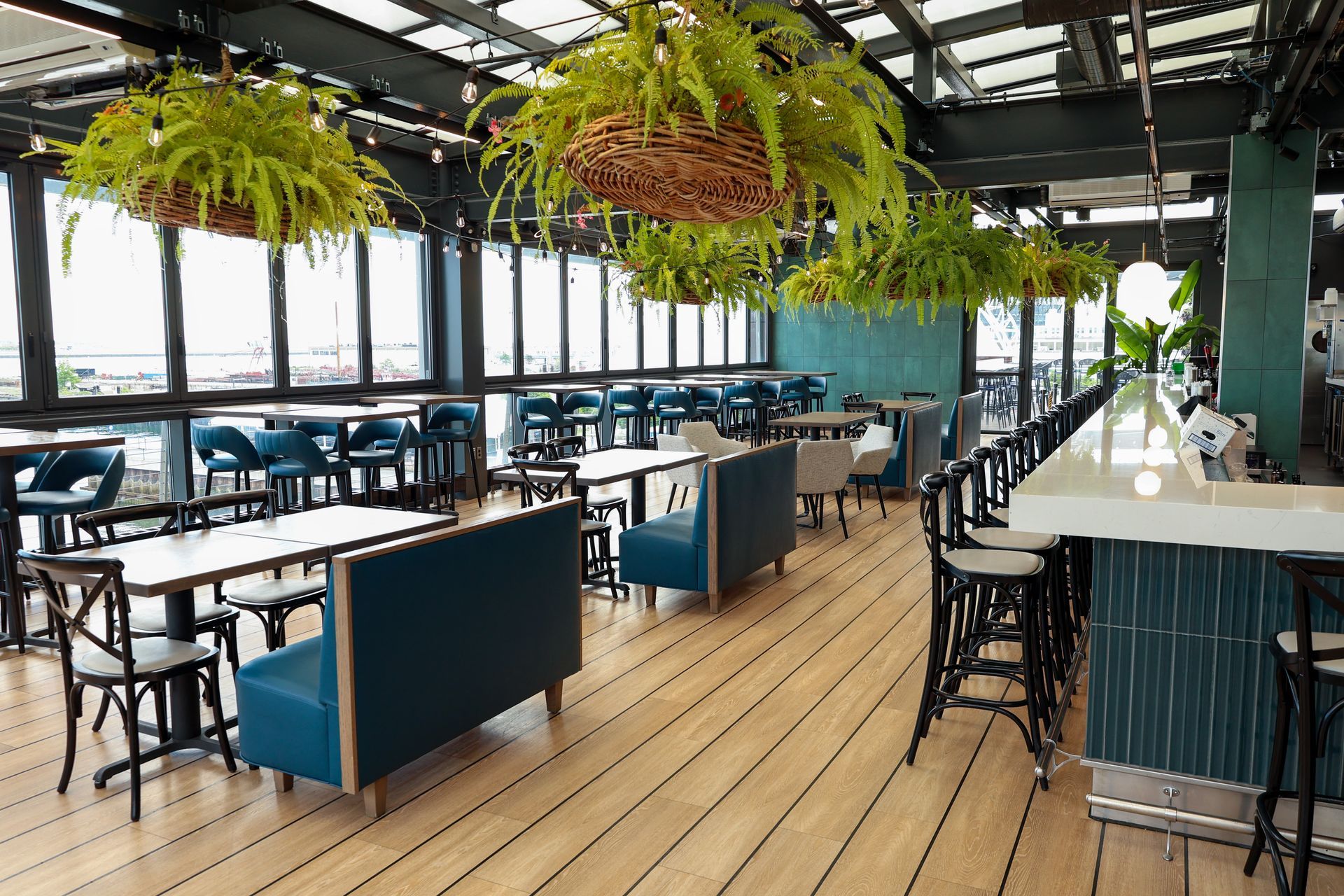 Open-air restaurant with blue booths, black tables, and hanging ferns under a glass roof