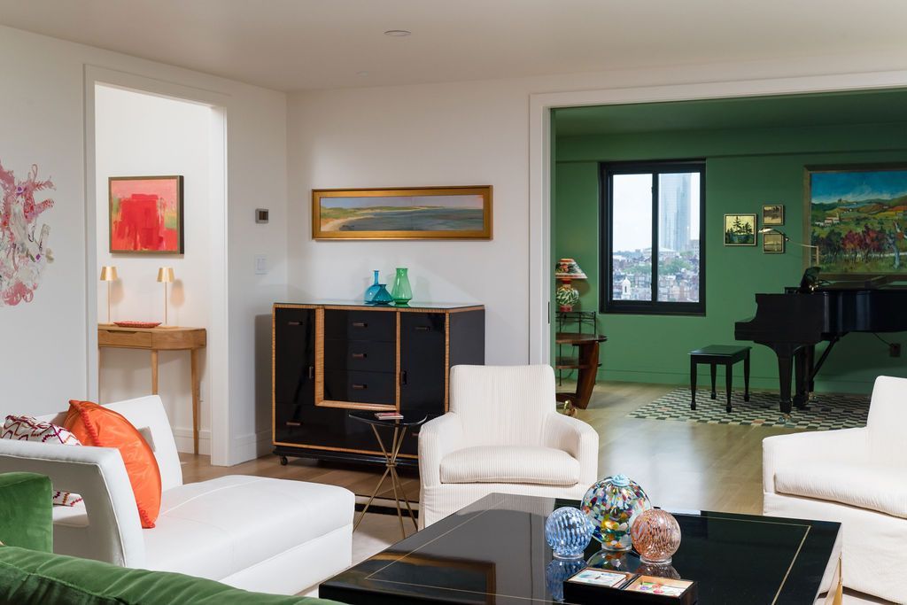 Modern living room with white sofas, black coffee table, and a green dining room in the background