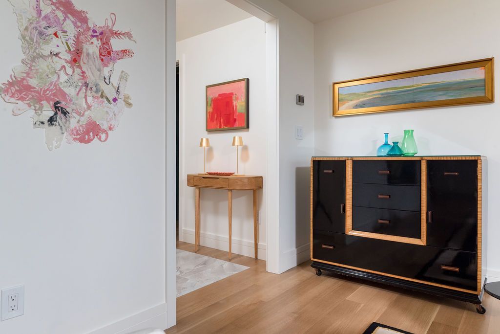 Modern living room with abstract wall art, wood console, and framed painting in a bright hallway.